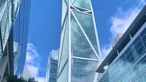 The glass shaft and white diagonal braces of 181 Fremont against a clear blue sky, framed by neighboring office facades. No people appear.