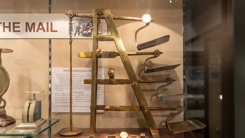 A brass postal ladder scale behind glass in a museum case. No people appear.