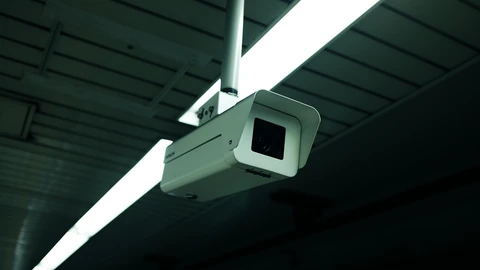 A white dome ceiling surveillance camera against a white ceiling. No people appear.