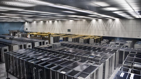 Long aisle of densely packed server racks inside a data center, with cable trays above. No people appear.