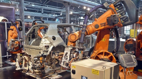 Several orange industrial robots arranged around a car-body welding cell in a museum exhibit. No people appear.