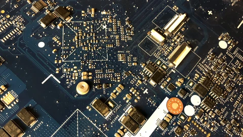 Close-up of a green circuit board with chips, capacitors, and solder pads. No people appear.