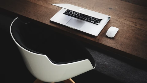 An empty wooden desk with an open laptop, notebook, and lamp after work. No people appear.