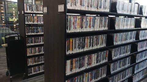 Tall library shelves filled with DVD cases in an empty aisle. No people appear.