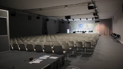 An empty conference room with rows of tables, chairs, and microphones under warm lighting. No people appear.