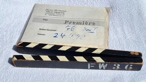 Wooden black-and-white striped clapsticks resting on a film label marked Première. No people appear.