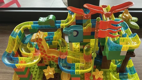 A colorful plastic marble-run track on a wooden floor with marbles in the channels. No people appear.