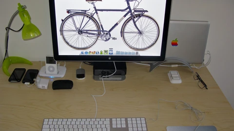 A desk with dual monitors, a keyboard, and a notebook in an empty room. No people appear.