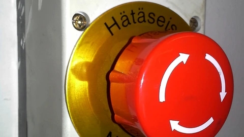 A red industrial emergency-stop button labeled in Finnish and Swedish. No people appear.