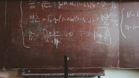 Close view of chalk mathematical formulas written across a worn blackboard surface. No people appear.