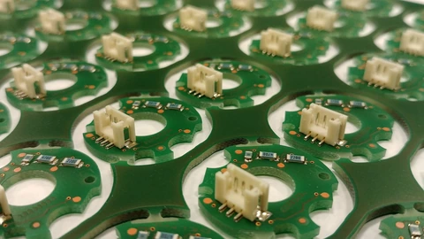 A manufacturing sheet of green printed circuit boards with copper traces, photographed from above. No people appear.