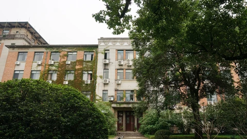 Three-storey teaching building with white walls and blue-framed windows on Zhejiang University’s Yuquan campus, photographed from a paved courtyard with orange trees.