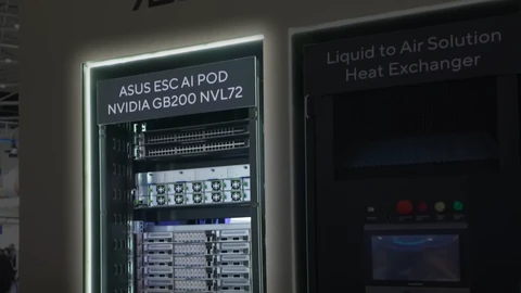 A lit black server rack labelled “ASUS ESC AI POD NVIDIA GB200 NVL72”, filled with network switches and compute trays, next to a cabinet labelled “Liquid to Air Solution Heat Exchanger”.