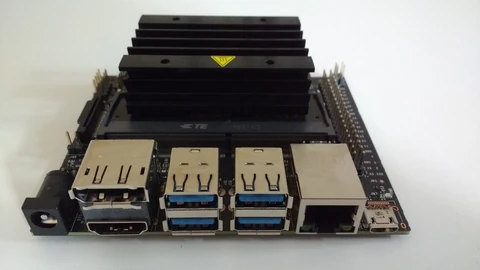 Front view of an NVIDIA Jetson Nano developer board, a small green circuit board with a large black heatsink, four USB ports, HDMI, DisplayPort and an Ethernet socket, on a white background.
