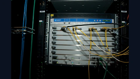 A modular network switch chassis in a black rack, its line cards lit by small green lights, with bundles of yellow fibre-optic patch cables and a blue cable plugged into the front.