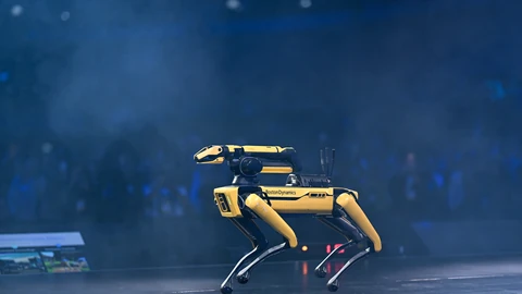 A yellow-and-black four-legged robot walking across a dark, misty stage under blue light.