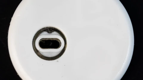 The underside of a small white, coin-shaped glucose sensor on a black background, with an oval opening in the middle where the sensor filament sits.