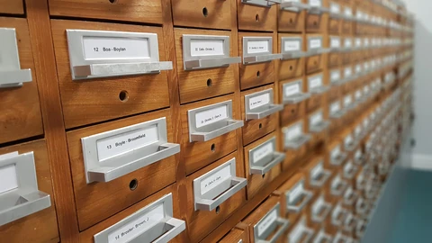 A tall wooden card filing cabinet with many small labeled drawers, photographed indoors.