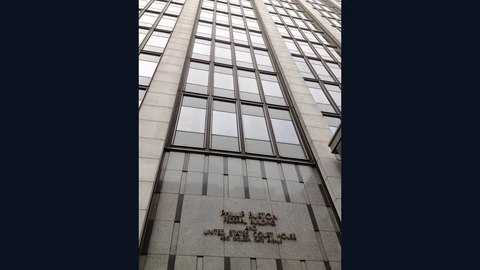 Looking up at the Phillip Burton Federal Building and United States Courthouse in San Francisco, a tall grey stone tower with rows of dark windows and its name in metal letters above the entrance, under a cloudy sky.
