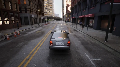 A grey sedan seen from behind drives down a wet city street lined with brick buildings, traffic cones and pedestrians on the pavements.