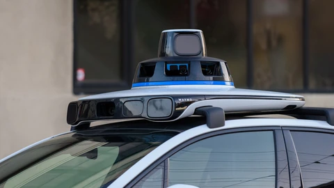 Close-up of the sensor dome on the roof of a white Waymo car, with a spinning lidar unit on top, a ring of cameras and a front sensor bar.