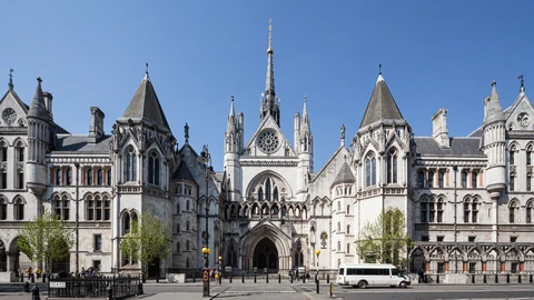 The Gothic stone front of the Royal Courts of Justice on the Strand in London, with a central arched entrance, a tall spire and turrets under a clear blue sky.