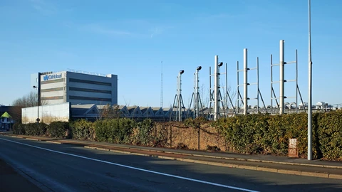 An OVHcloud-branded building at the Roubaix site with rows of tall metal exhaust stacks and rooftop equipment behind a hedge beside an empty road.
