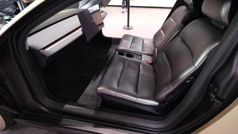 Inside a Tesla Cybercab concept: a two-seat bench in dark leather with cup holders between the seats, facing a dashboard with a single screen and no steering wheel or pedals.