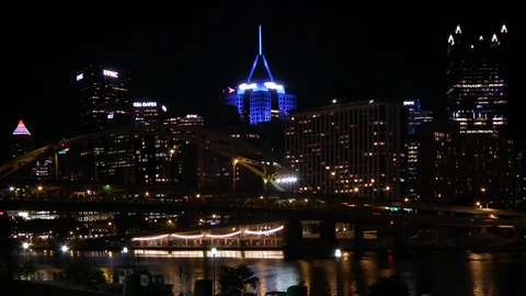 Downtown Pittsburgh towers seen from the North Shore under a blue sky. No identifiable people appear.
