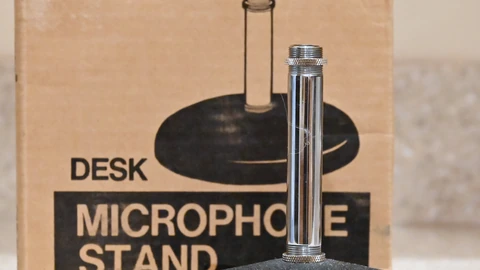 A silver desk microphone on a round stand against a dark background. No people appear.