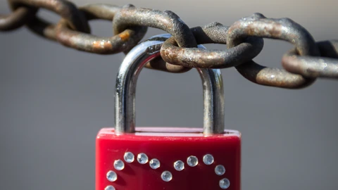 A brass padlock hanging on metal mesh against a blurred river background. No people appear.