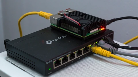 A Raspberry Pi 4 resting on a black network switch with blue Ethernet cables. No people appear.