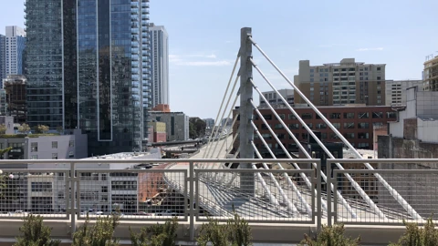 Empty white cable-stayed bus ramp at the Salesforce Transit Center, with a mesh railing in the foreground and downtown towers behind. No people appear.