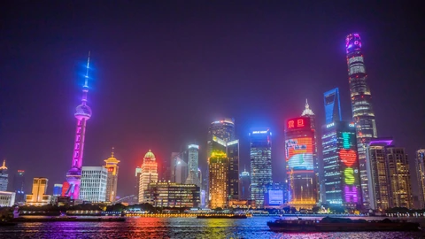 Night panorama of Shanghai’s Lujiazui towers lit in blue and gold across the river. No identifiable people appear.