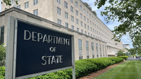 A black DEPARTMENT OF STATE sign in raised letters beside a hedge and the pale stone Truman Building, with empty lawn at right. No people appear.