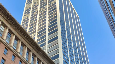 Spear Tower’s white shaft and grid of windows against a clear blue sky, with a brick cornice and columns at lower left. No people appear.