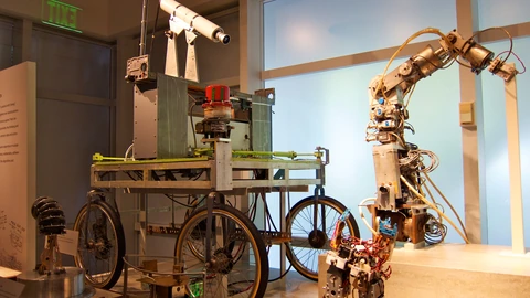 Historic Stanford Cart vehicle beside a hydraulic robot arm in a workshop. No people appear in frame.