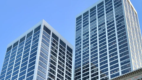 The upper shafts of two white office towers with dark window grids against a clear blue sky. No people appear.