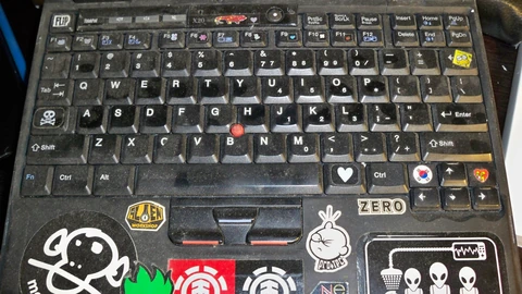An open ThinkPad laptop on a wooden table beside a mouse and notebook. No people appear.