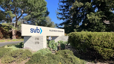 White roadside sign reading SVB and Kleiner Perkins at 27500–27700 Sand Hill Road, with hedges and trees and no people.