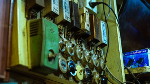 A wall-mounted electrical switchboard with ceramic fuses and rows of toggle switches. No people appear.