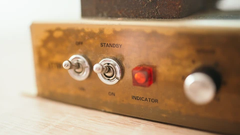 Close-up of vintage metal toggle switches and an amber indicator light on a control panel. No people appear.