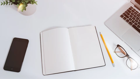 An open laptop on a white desk beside a notebook and phone. No people appear.