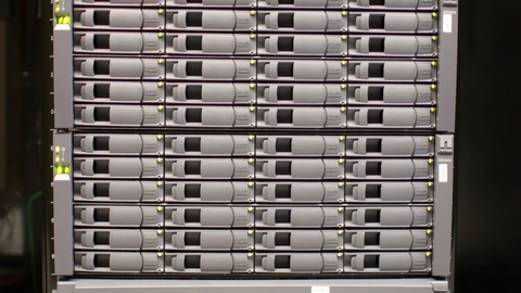 Corridor of server racks with green status lights in a data center. No people appear.