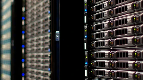 Rows of server racks with blue network cables in a brightly lit data hall. No people appear.