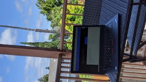 A ThinkPad laptop open on a wooden desk, photographed from above in shadow. No readable screen content and no people.