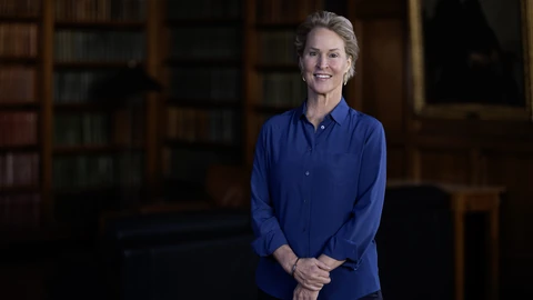 Frances Arnold standing with hands clasped in a dark wood-paneled library, wearing a blue shirt.