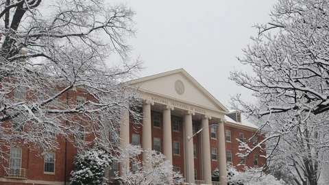 The National Institutes of Health Building 1, a brick building with a white-columned portico and snow-covered trees, photographed in winter.