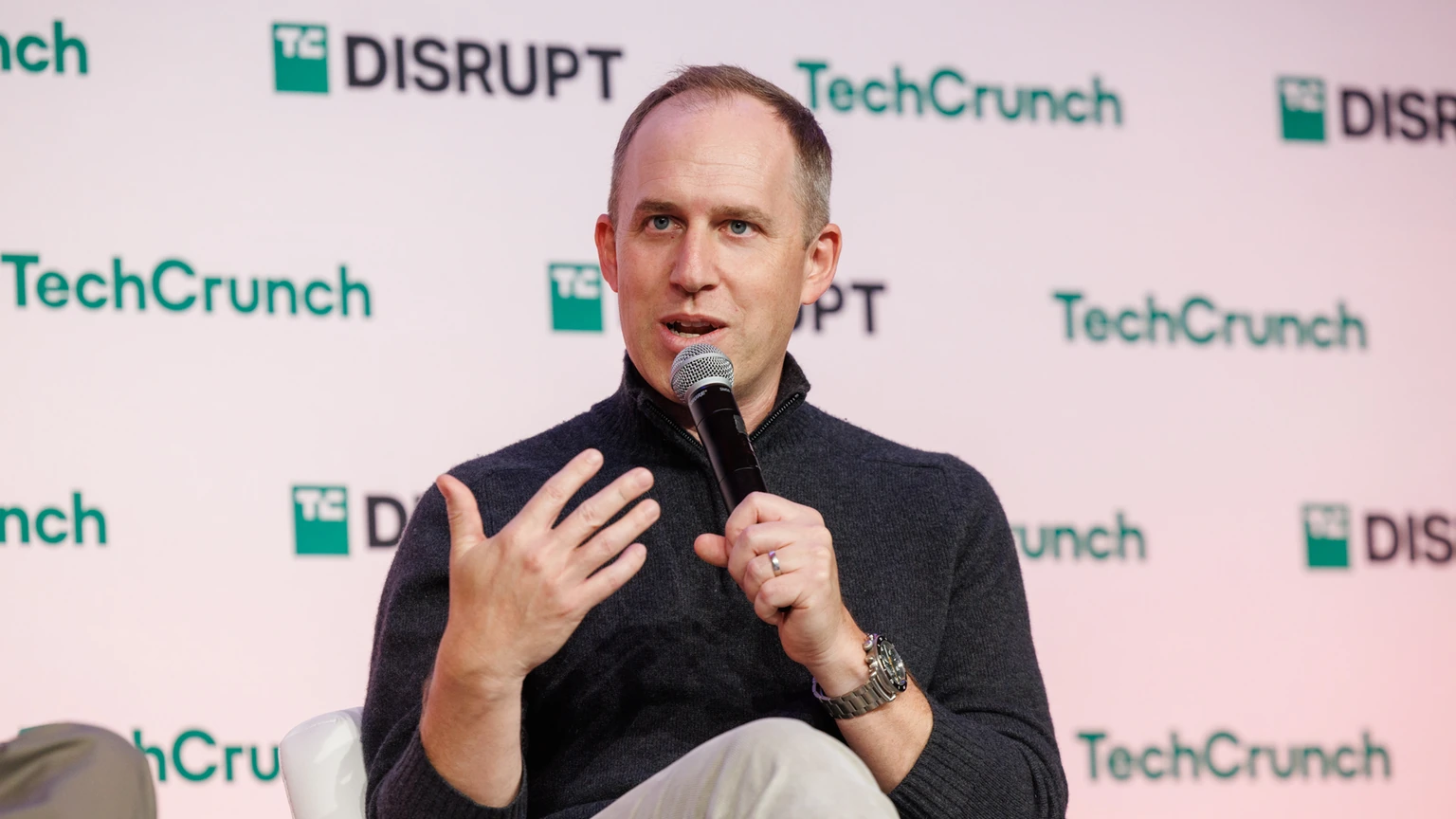 Sierra co-founder Bret Taylor holding a microphone and gesturing while speaking on a TechCrunch Disrupt stage.