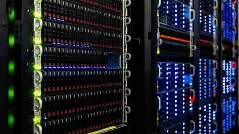 Close-up of a white server rack filled with black drive bays and small status LEDs, with a second rack of blue lights out of focus to the right.